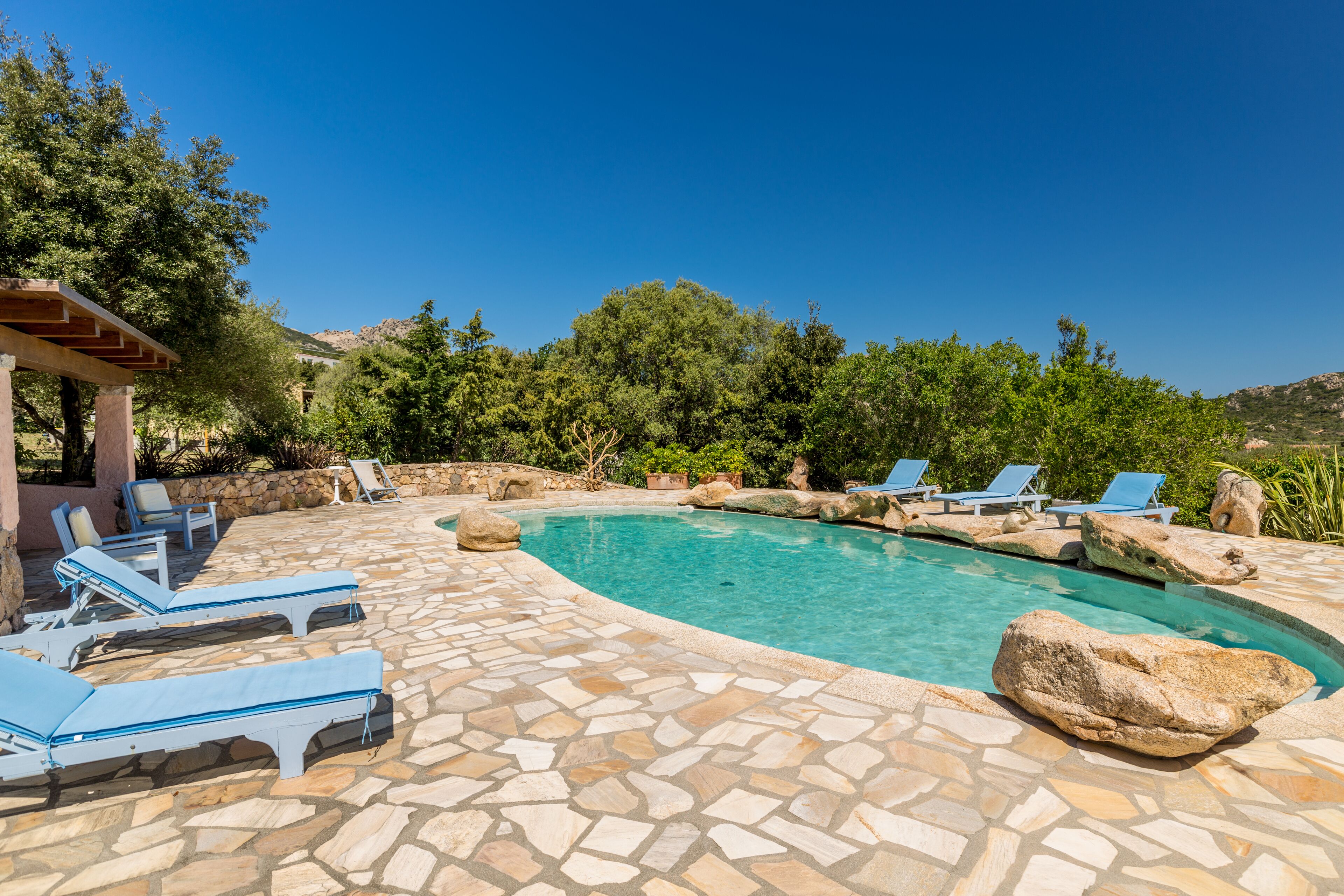 A pool area with stone flooring, lounge chairs, and a pergola.
