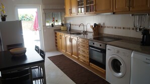 A kitchen with wooden cabinets, a sink, a washing machine, and a dining area with a table and chairs. - SEASIDE VILLA WITH PRIVATE SWIMMING POOL  (Manta Rota)