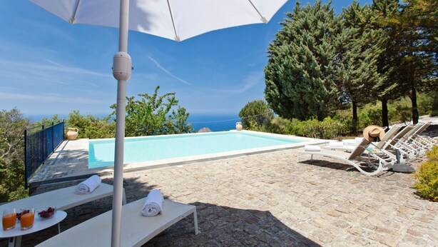 A poolside area with lounge chairs, a table with towels, and a view of the sea.