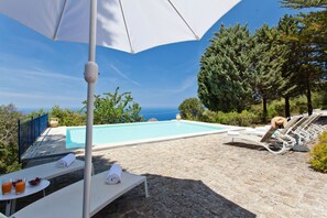 A poolside area with lounge chairs, a table with towels, and a view of the sea. - Villa Rocca - Holiday Rental with private swimming pool in Cefalù, Sicily (Cefalù)