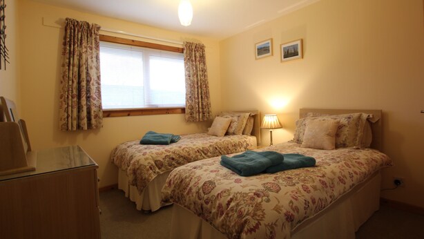 A bedroom with two beds, a desk, and a window with curtains. - An Airigh  - within walking distance from Stornoway (Stornoway, Isle of Lewis, Scotland)