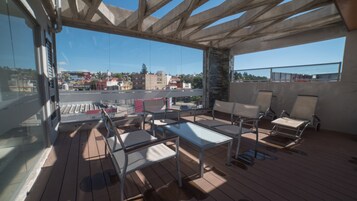Un balcón con piso de madera, sillas de metal, una mesa y vistas a edificios y árboles.