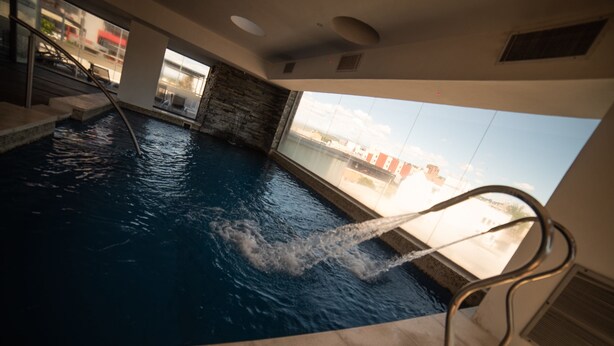 An indoor swimming pool with a view of the cityscape through large windows. - Hotel Estilo MB (Villa Carlos Paz)