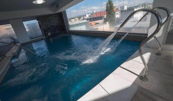 Una piscina interior con agua cristalina, una pared de piedra y vistas a edificios.