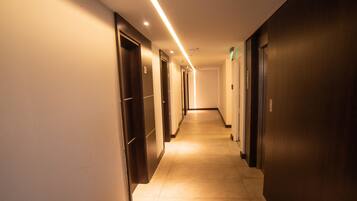 A long, narrow hotel corridor with doors on both sides, illuminated by overhead lighting.