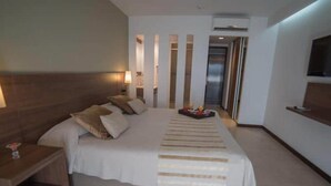 A modern hotel room with a large bed, bedside tables, a TV, and a bathroom visible through a sliding door. - Hotel Estilo MB (Villa Carlos Paz)