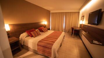 Habitación de hotel con cama, mesitas de noche, escritorio, silla, televisión y ventana con cortinas.