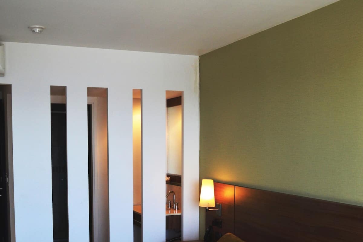 A hotel room with a large bed, a nightstand with a lamp, and a view of the bathroom through a door.