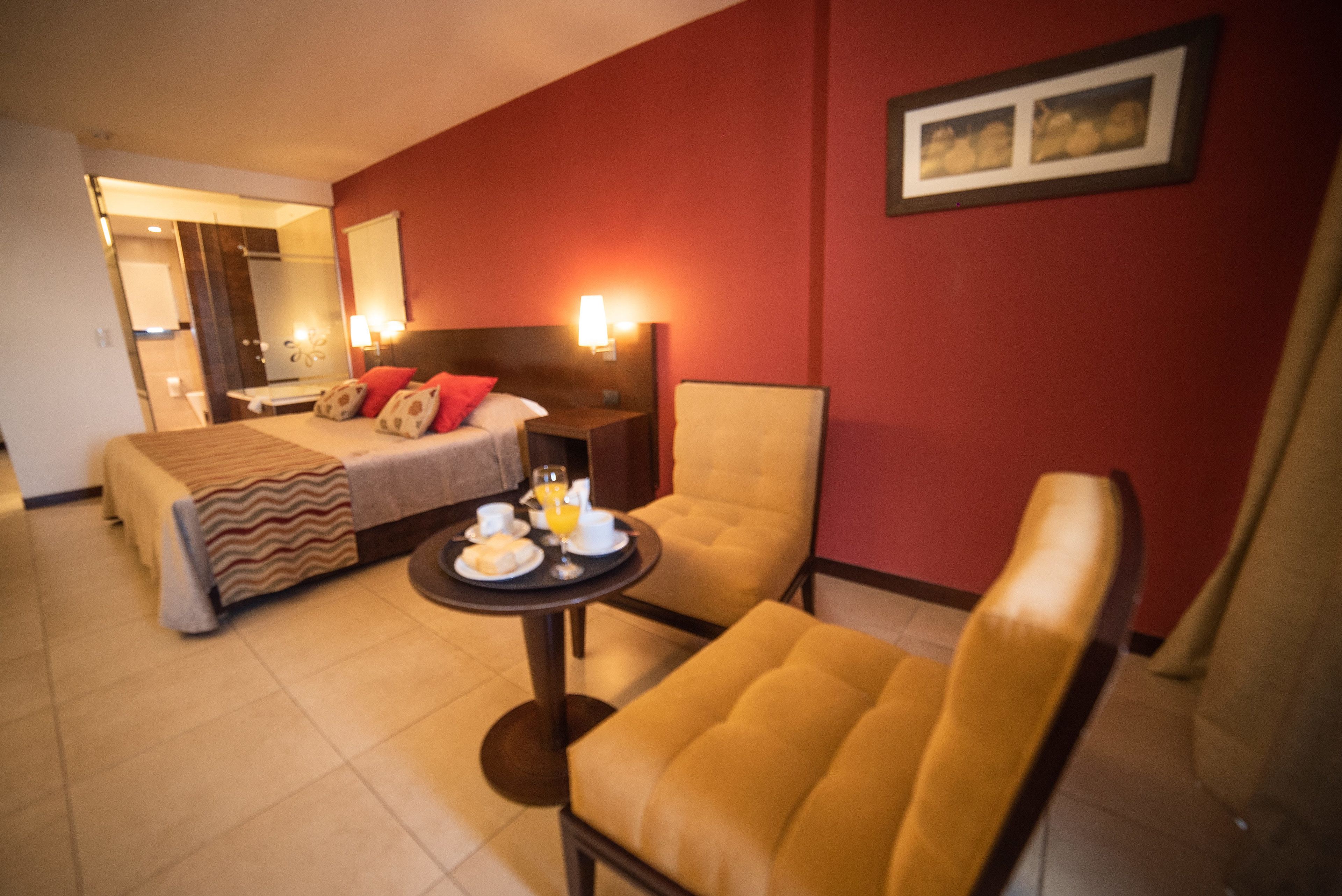 Une chambre d’hôtel avec un lit, une chaise, une table avec le petit-déjeuner, et une salle de bain visible à travers une porte ouverte.