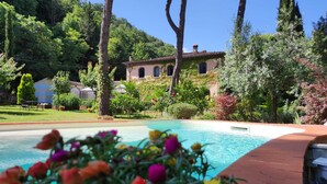 Une piscine entourée d’une végétation luxuriante et une villa avec un toit en tuiles.