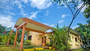 A house with a covered patio, surrounded by lush greenery and a clear blue sky. - CASA ANACAHUITA, Limonal, Jarabacoa (Jarabacoa)