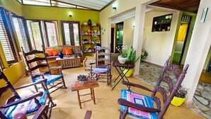 A cozy living area with wooden furniture, a sofa, and a coffee table. There are potted plants and a bookshelf with various items. - CASA ANACAHUITA, Limonal, Jarabacoa (Jarabacoa)