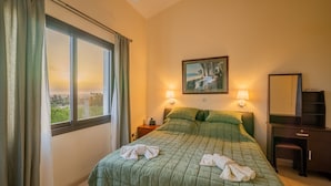 Quarto de hotel com uma cama grande, duas luminárias laterais, um quadro na parede e vista para o campo pela janela.