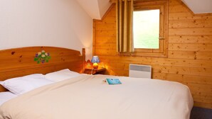 Een knus slaapkamer met een houten hoofdbord, een bed met witte beddengoed, een nachtkastje met een lamp en een raam met gordijnen.
