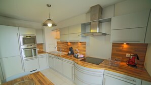 Eine moderne Küche mit weißen Schränken, Edelstahlgeräten, einer Holz Arbeitsplatte und einem eingebauten Backofen.