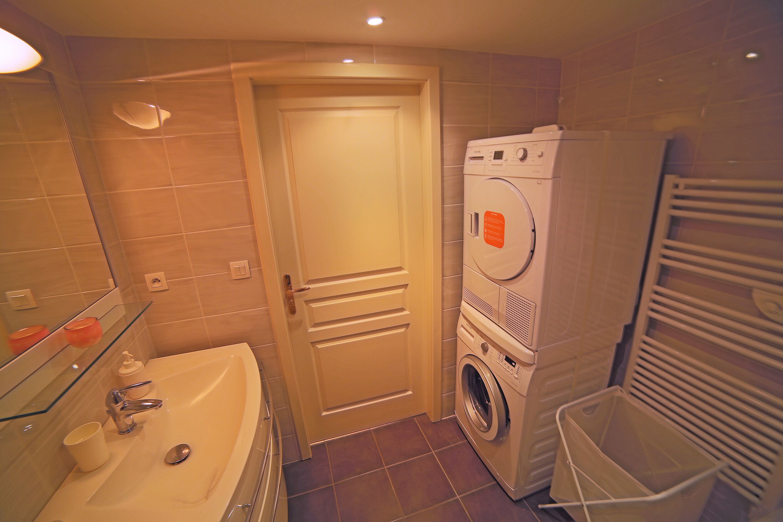 A compact bathroom with a sink, mirror, and a stacked washer and dryer.