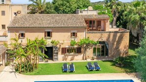 Una casa a due piani con piscina, un giardino con palme e una terrazza con poltrone relax.