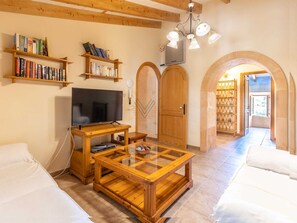 Una sala de estar acogedora con televisor, estanterías de madera con libros, una mesa de centro de vidrio y una puerta de madera.