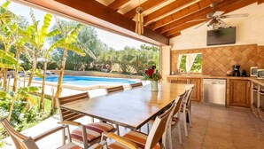 Un'ampia cucina con un piano di lavoro in legno, una zona pranzo con sedie a righe e un'ampia finestra vista piscina.