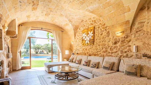 Una stanza con pareti in pietra, un divano, un tavolino da caffè e vista su una piscina.