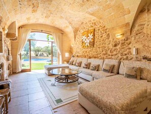 A stone-walled room with a sofa, a coffee table, and a view of a pool.
