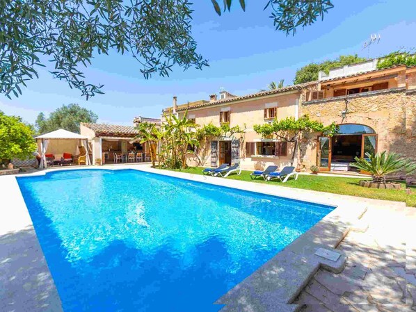 Vista de la piscina de una villa, con sillones de descanso y un patio cubierto.