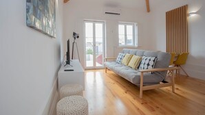 Un salón moderno con un sofá gris, suelo de madera y un ventanal grande.