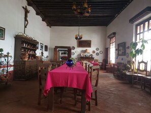 A dining area with a long table covered in a bright pink tablecloth, wooden chairs, and a chandelier. - Ex-Hacienda San Buenaventura (Tlaxco)