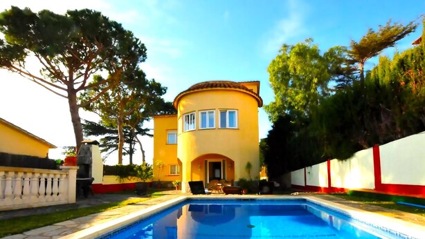 A swimming pool with a clear blue water surface, surrounded by a well-maintained lawn and a yellow building with a curved roof.