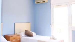 A hotel room with two beds, a wooden nightstand, a white bedside table, a brown pillow, and an air conditioning unit on the wall.