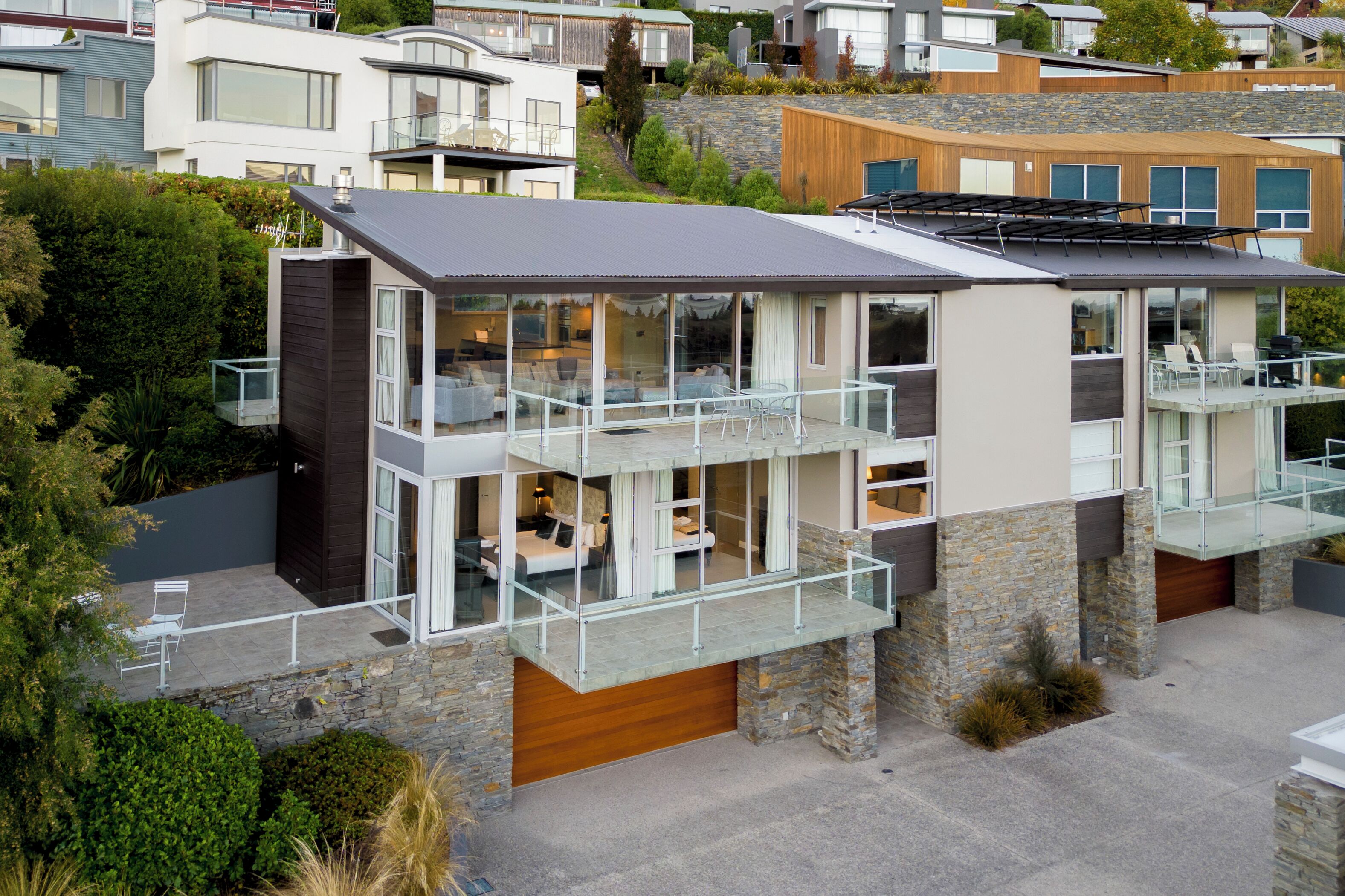 Une maison moderne à plusieurs étages, dotée de grandes fenêtres en verre, d’un balcon et d’un garage.