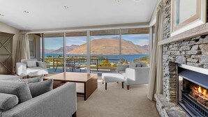 A spacious living room with a fireplace, large windows offering a mountain and lake view, and a cozy seating area. - Remarkable Location – Queenstown (Queenstown)