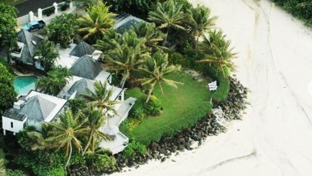 Propiedad costera con varias construcciones, piscina y palmeras.