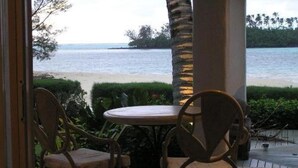 Vista desde un espacio exterior cubierto con una mesa y sillas, con vista a la playa y el océano.