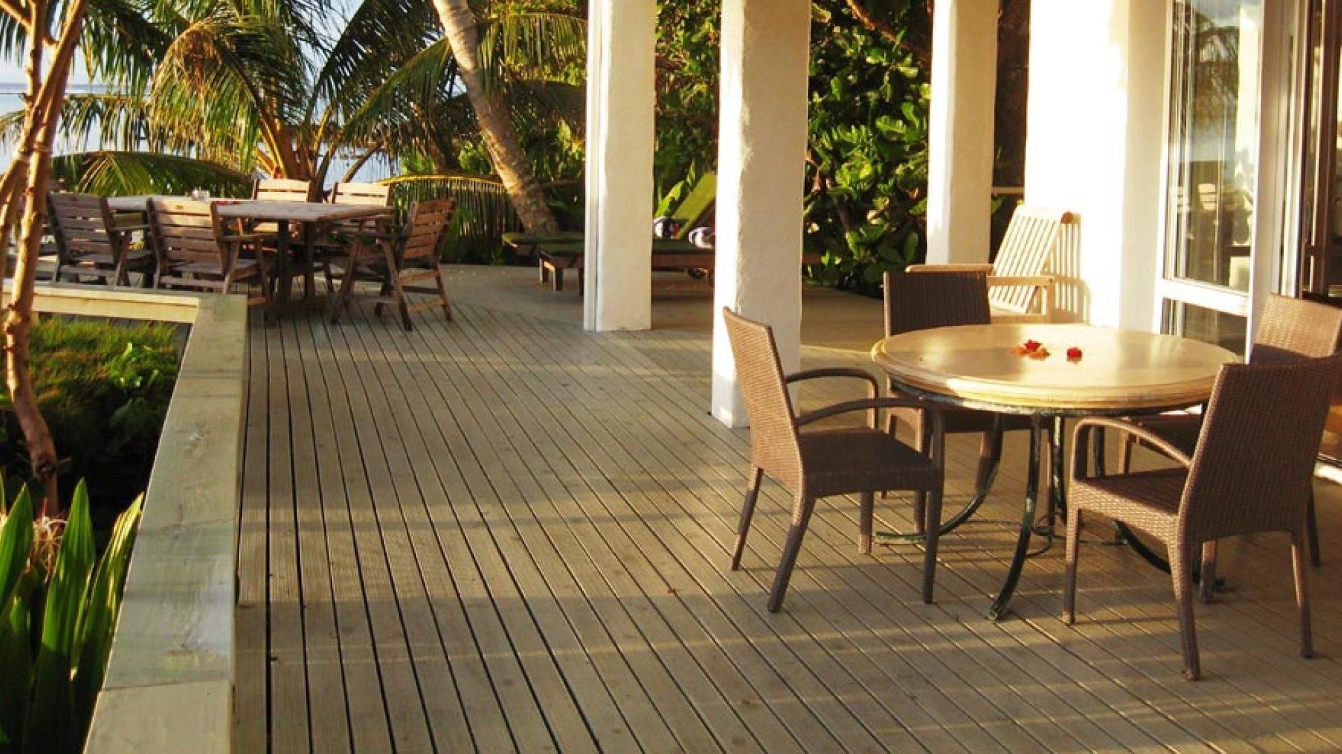 An outdoor patio with wooden flooring, round tables, and wicker chairs.