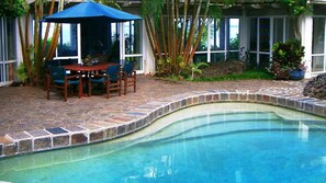 A pool with a stone border, a table with chairs, and a blue umbrella.