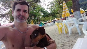 En man håller i en hund på en strand med vita och gula stolar och parasoller.