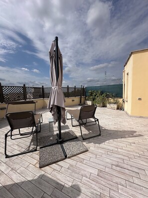 Un patio al aire libre con dos sillones de descanso, una mesa y una sombrilla.