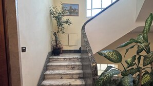 Una escalera de mármol con barandilla, plantas en macetas y un cuadro en la pared.