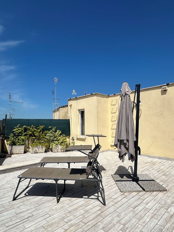 A rooftop terrace with a table and chairs, a covered umbrella, and potted plants.