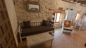 Una habitación acogedora con pared de piedra, un banco de madera, un armario blanco y suelo de baldosas.