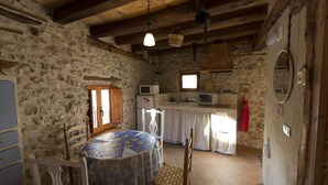 Una cocina rústica con paredes de piedra, vigas de madera, una mesa de comedor con sillas y un microondas.