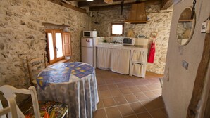 Una cocina rústica con paredes de piedra, techo de madera y servicios básicos, incluyendo un refrigerador, microondas y pileta.