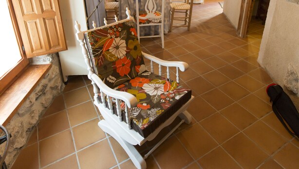 Una cocina rústica con paredes de piedra, vigas de madera, un refrigerador blanco, un microondas y una silla de madera con cojín floral.
