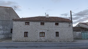 Un edificio de piedra con techo de tejas, dos ventanas y una puerta pequeña.
