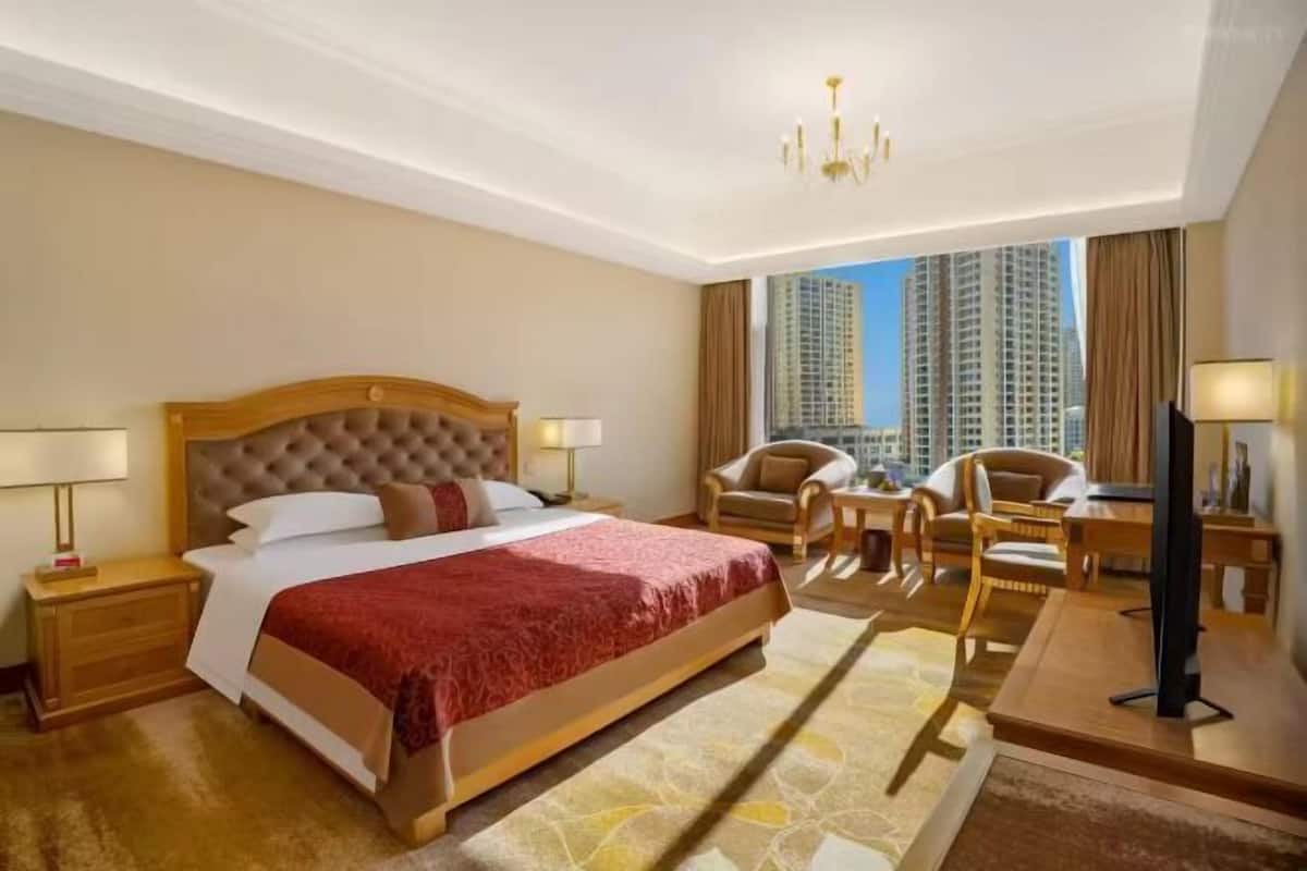 A hotel room with a large bed, a desk with a chair, a television, and a view of tall buildings.