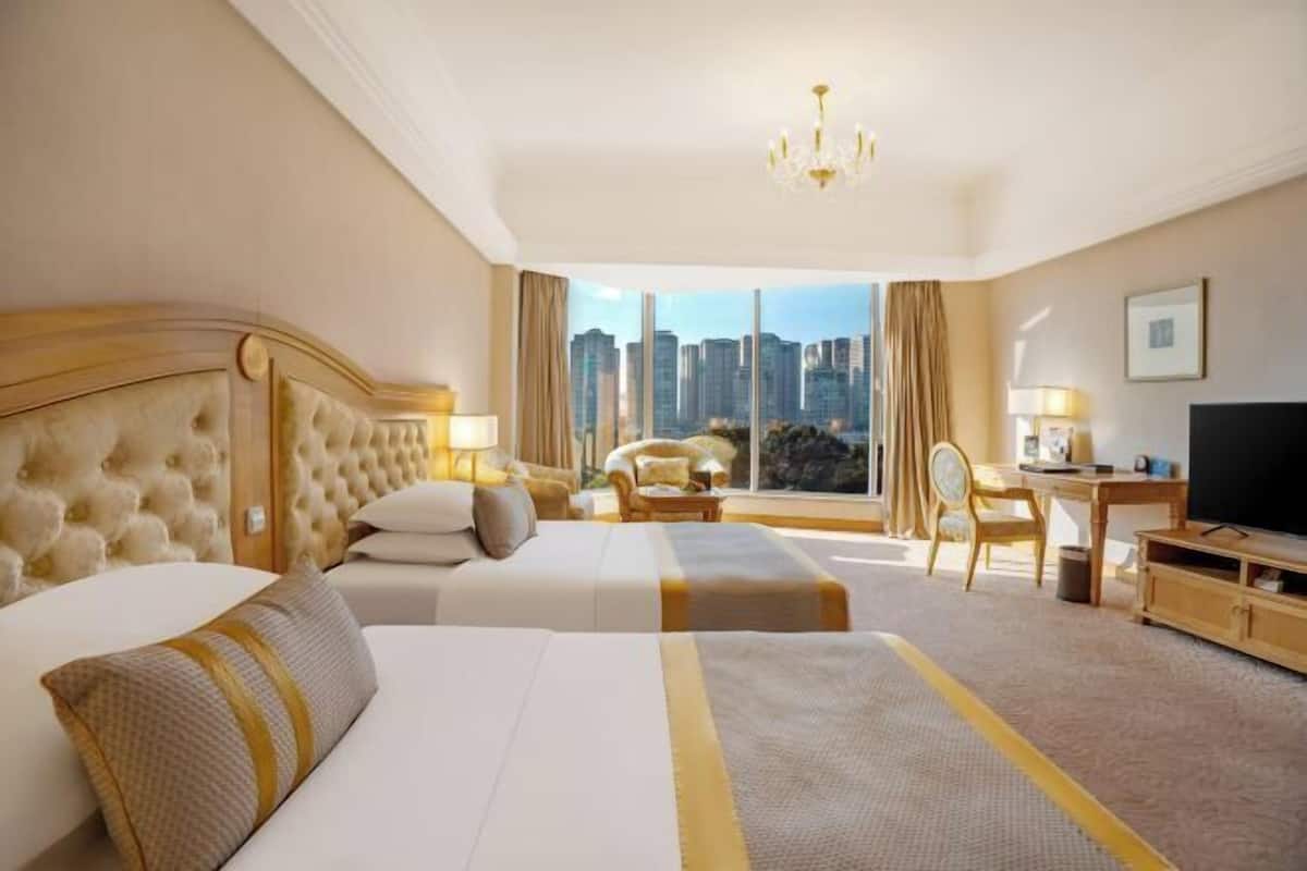A hotel room with a large bed, a smaller bed, a desk, a chair, and a TV.