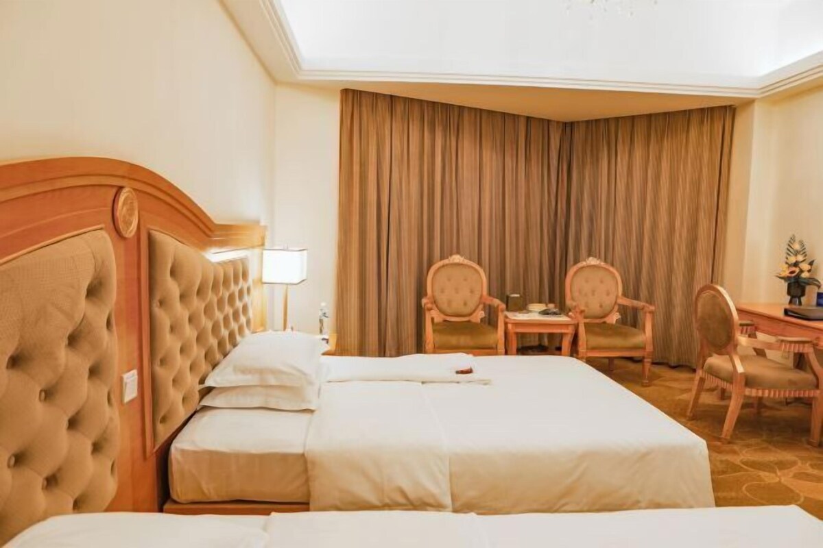 Una habitación de hotel con una cama grande, dos sillas, un escritorio y un telón de fondo.