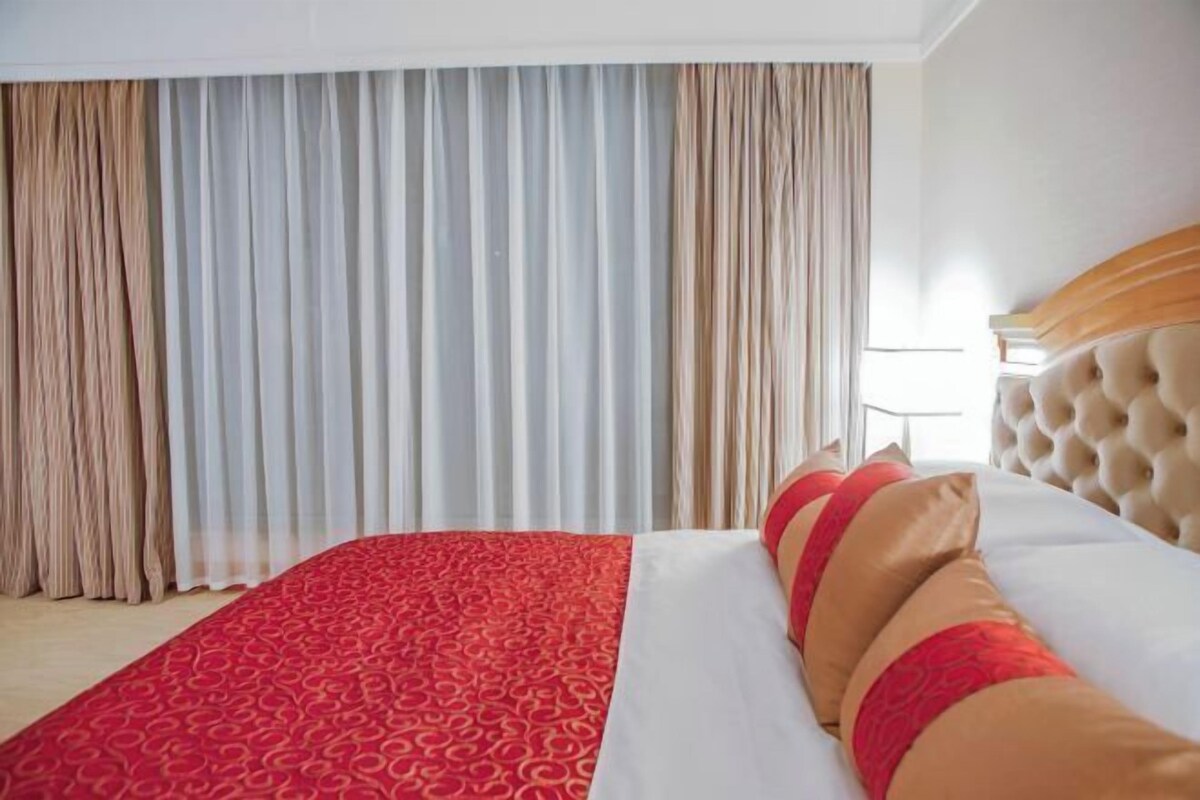 Una habitación de hotel con una cama grande, cabecera color crema y colcha estampada roja.
