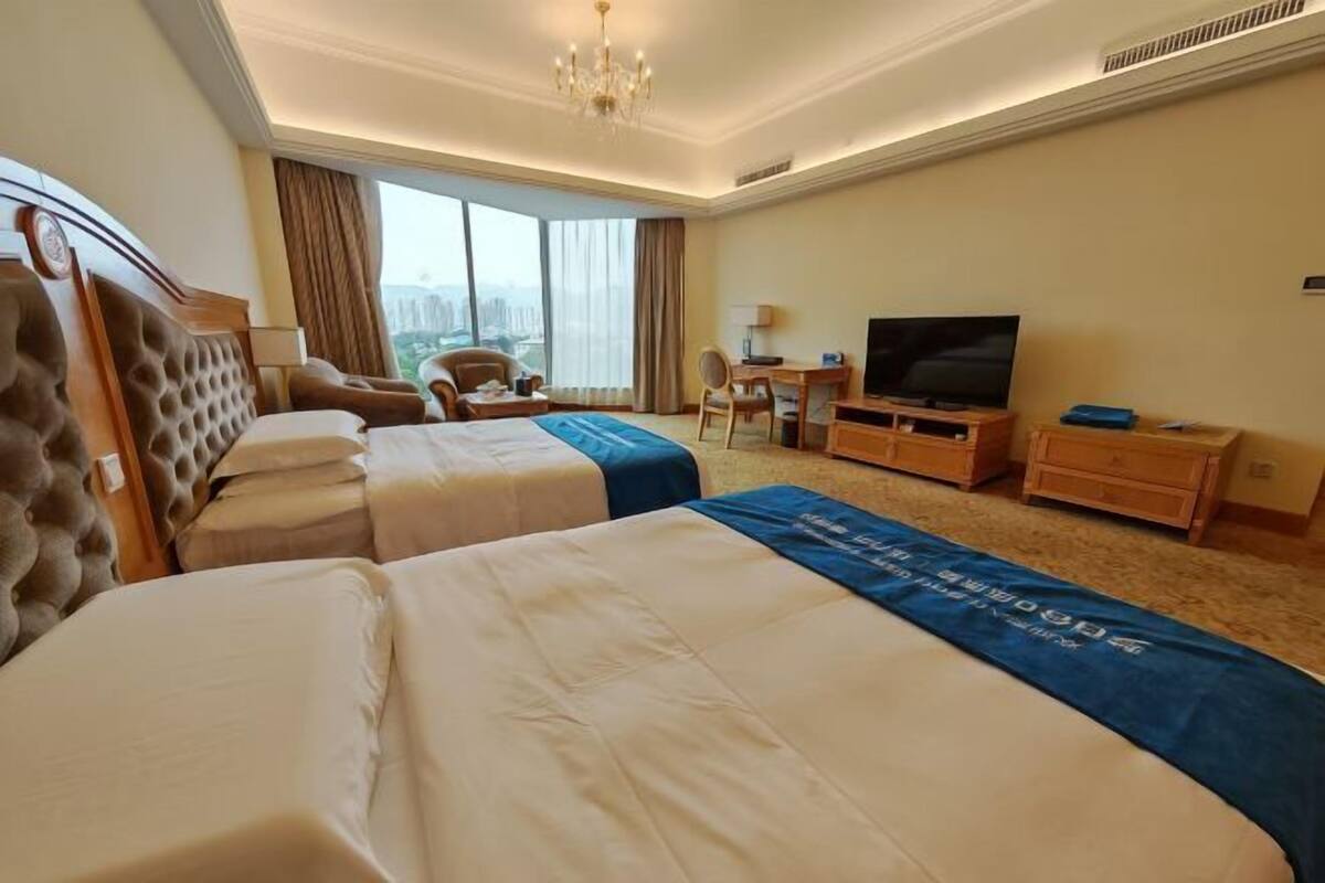 A hotel room with two beds, a television, a desk, and a chair.